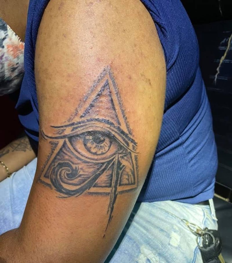 Black and grey tattoo of an eye inside a pyramid on an upper arm.