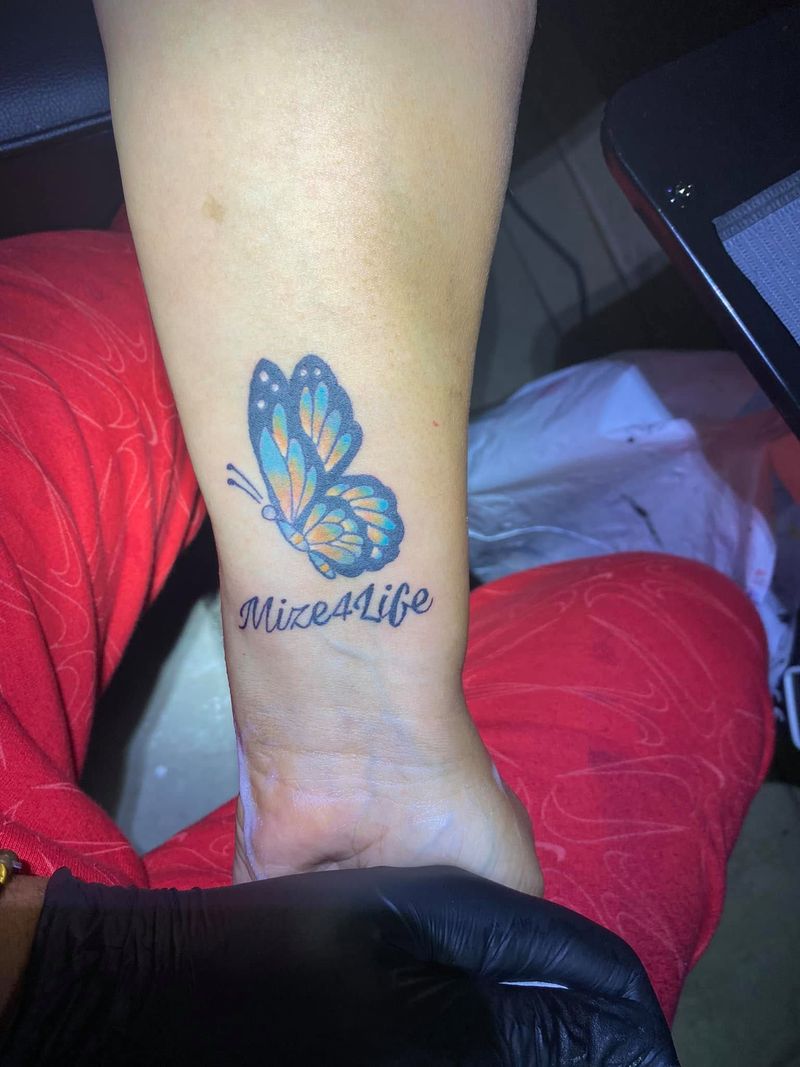 Blue butterfly tattoo above a line of script on the inner forearm.