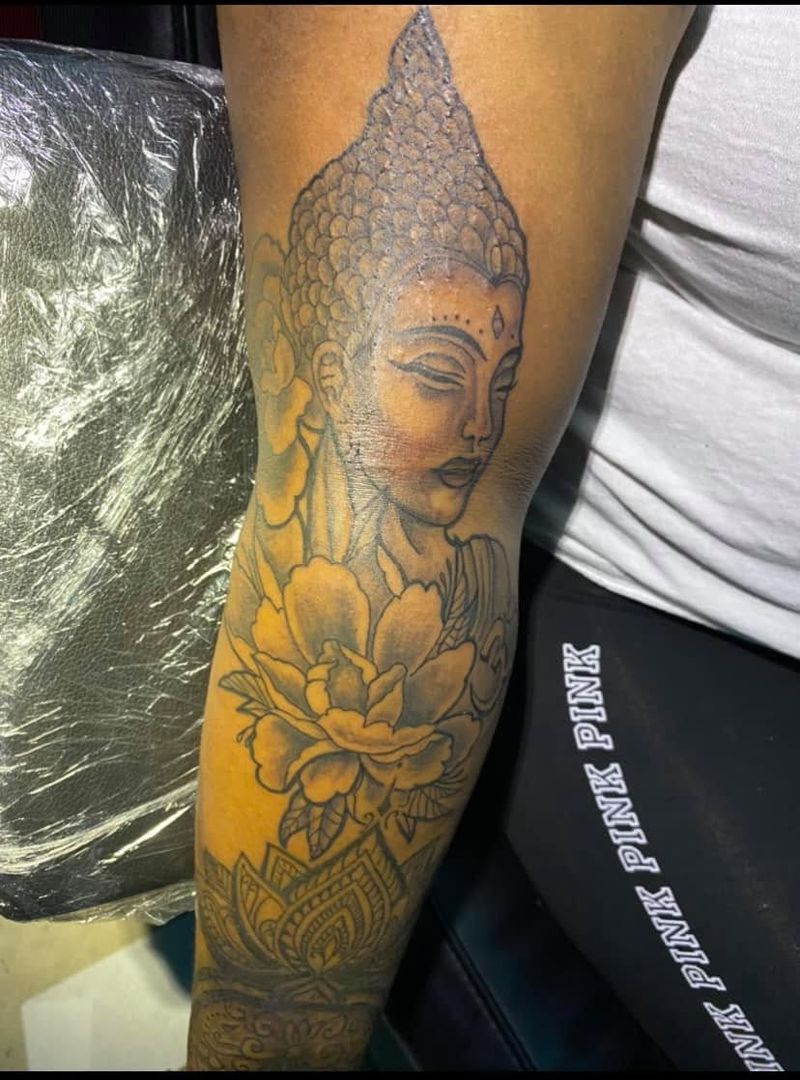 Black and grey tattoo of a Buddha head above a lotus flower on a forearm.