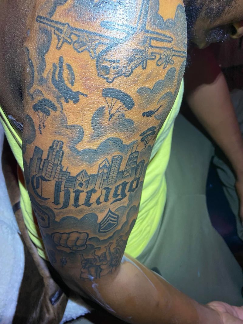 Black and grey half sleeve tattoo with airplanes, parachutes, clouds and a city skyline above the word Chicago in bold script.