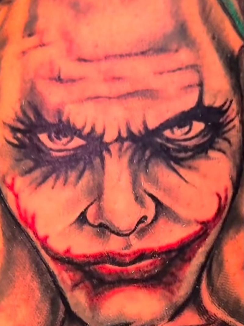 Close-up portrait tattoo of a clown-faced villain with heavy dark eye shading and a red painted smile.