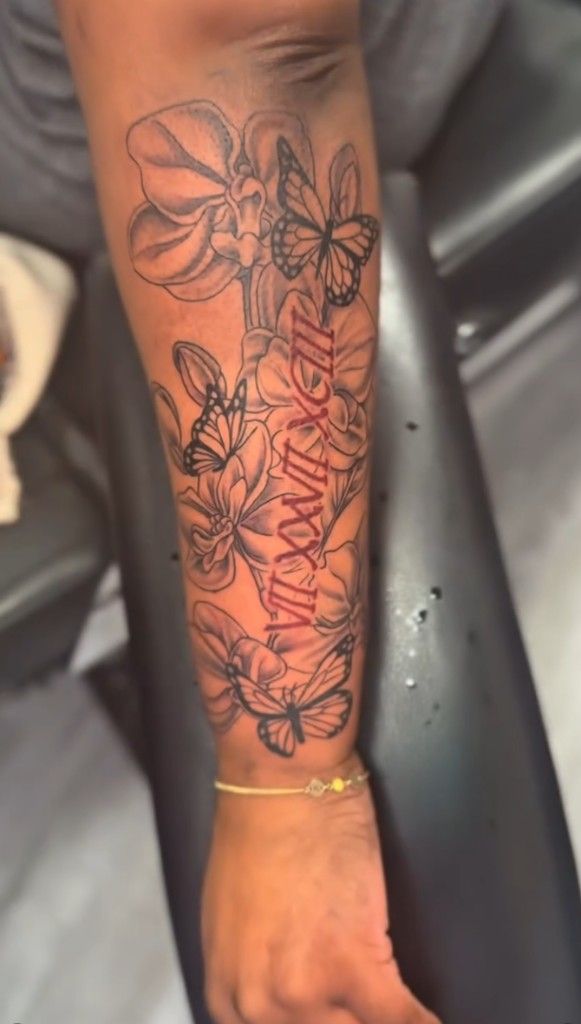 Forearm tattoo with flowers, butterflies and red Faith lettering running through the center.