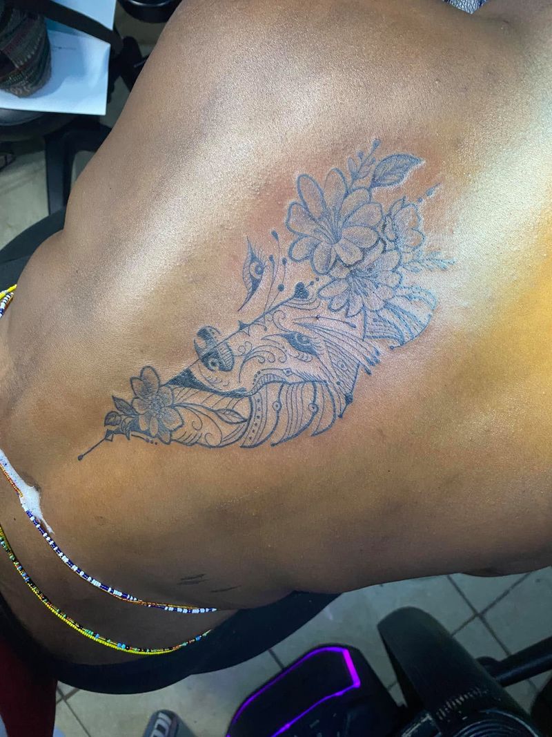 Black and grey tattoo of a feather with flowers on the side of the back.