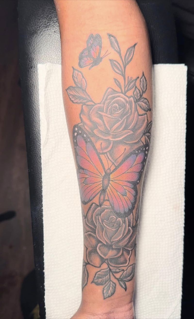 Forearm sleeve tattoo of shaded roses and leaves with an orange butterfly at its center.
