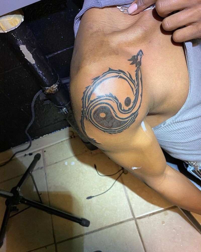 Black and grey yin yang tattoo with a curling tail on the shoulder.